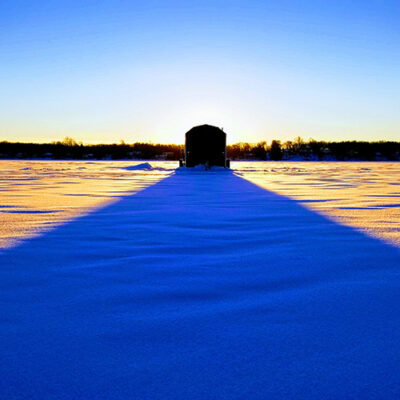 Sun rising over ice house casting a shadow on a frozen lake